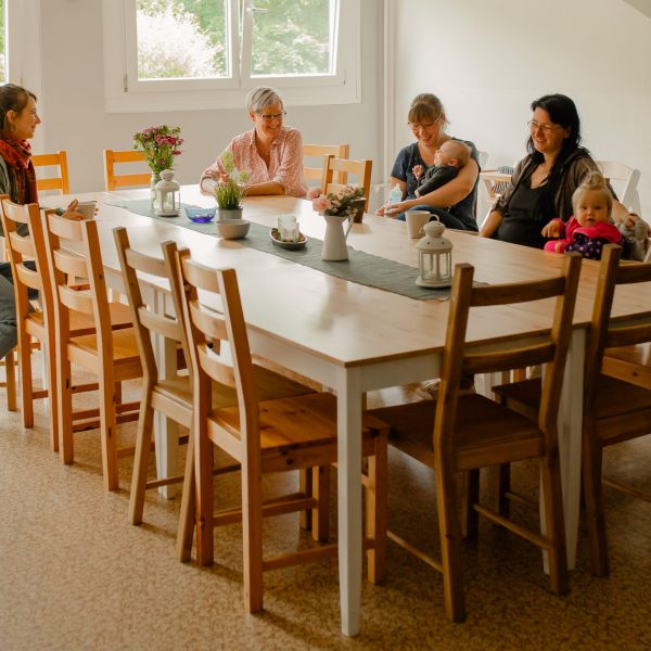 Frauen sitzen mit ihren Kindern am Tisch und lachen.