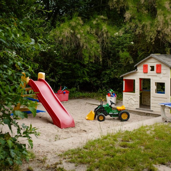 Ein Sandkasten mit kleiner Rutsche, kleinem Fahrzeug und Spielhaus.