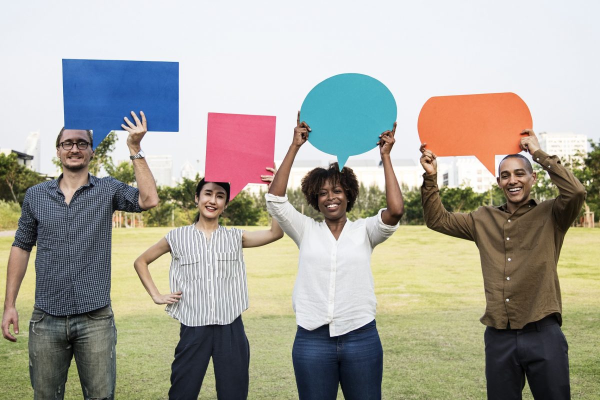 Personen, die eine Sprechblase hoch halten. Die Sprechblasen sind aus farbigen Papier ausgeschnitten.