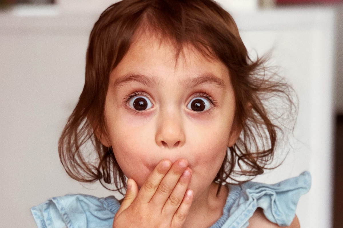 Ein Kind hält sich die Hand vor dem Mund und schaut erstaunt.
