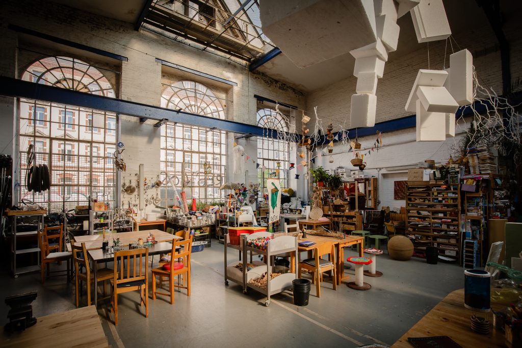 Restloshalle von innen mit Tischen, Stühlen, Regalen und Upcycling-Materialien.