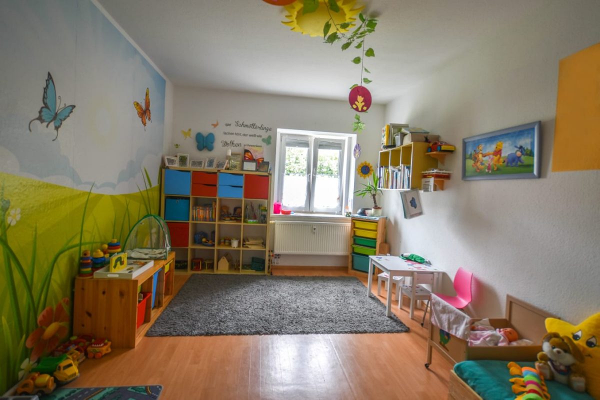 Buntes Kinderzimmer mit Regalen, Spielzeug und Sitzgelegenheiten.