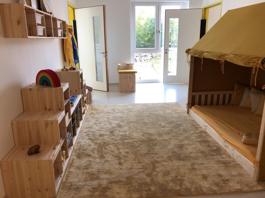 Ein heller Raum mit Kinder-Kuschelecke und Regalen mit Spielzeug.