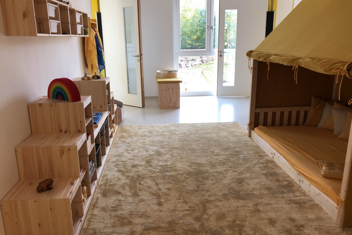 Ein heller Raum mit Kinder-Kuschelecke und Regalen mit Spielzeug.