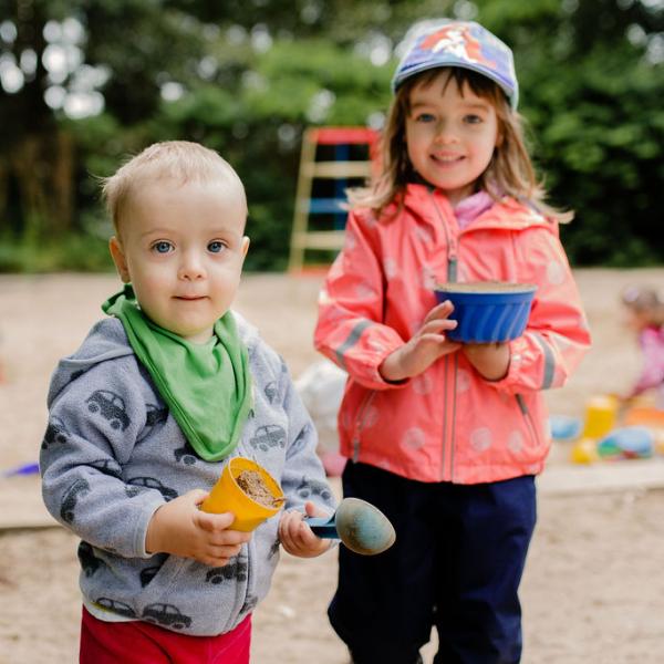 Zwei Kinder halten Sandformen in ihren Händen und lächeln uns an