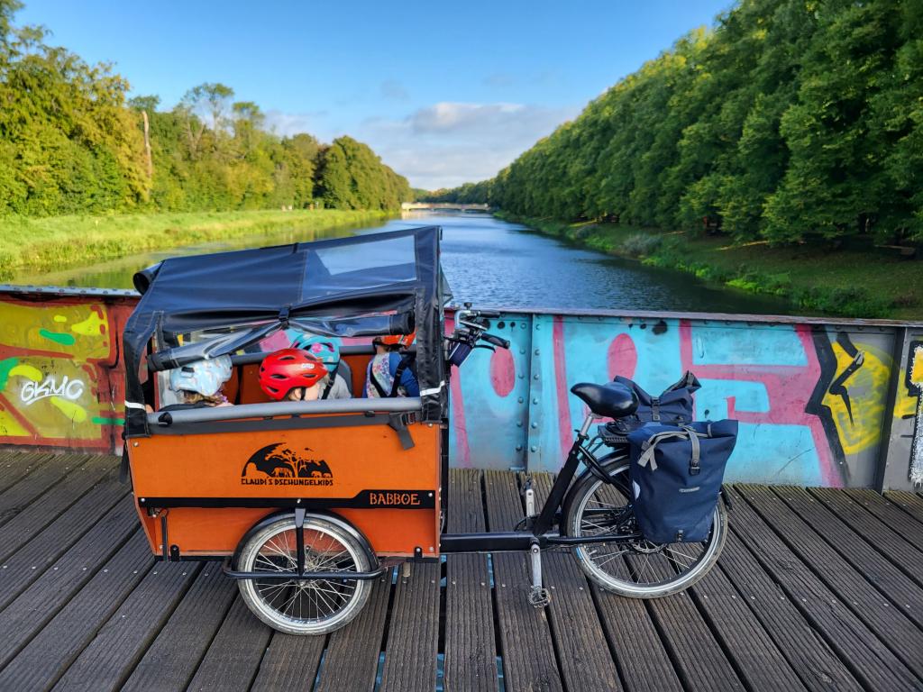 Ein Lastenrad für „Claudi's Dschungelkids“ - FiZ Leipzig Ein Lastenfahrrad steht auf einer Brücke. Darin sitzen vier Kinder mit Fahrradhelm.