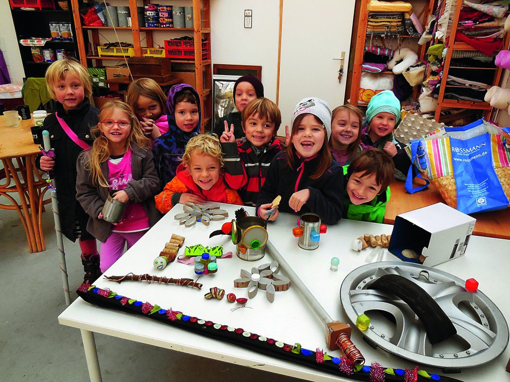 Viele Kinder stehen lächelnd hinter einem Tisch mit Upcycling-Gegenständen.