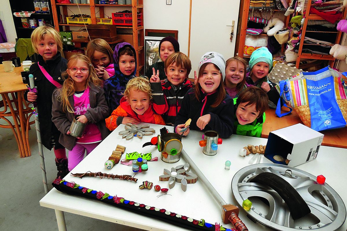 Viele Kinder stehen lächelnd hinter einem Tisch mit Upcycling-Gegenständen.