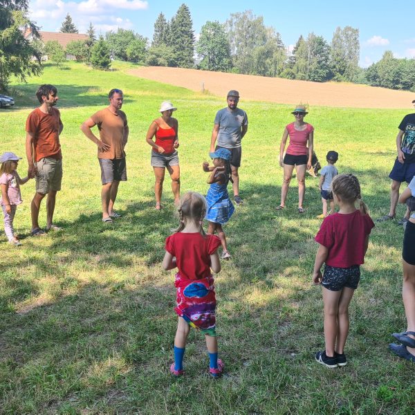 viele erwachsene Menschen und Kinder stehen in einem großen Kreis auf einer Wiese