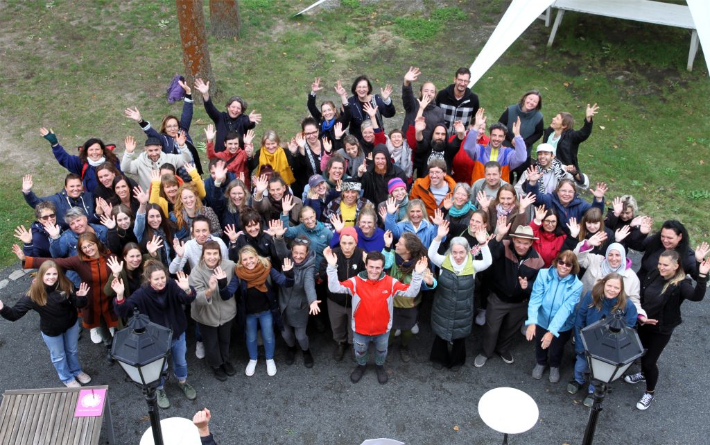 Ein Gruppenfoto der Mitarbeitenden des Mütterzentrum e.V. Leipzig, aufgenommen aus der Vogelperspektive: Personen unterschiedlichen Alters Lachen und Winken in die Kamera.