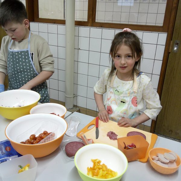 Kinder in der Paunsdorfer KiFaZ-Kita „Kleine Entdecker“ schneiden Paprika, Tomaten und Salami zum Belegen der Pizzen klein.