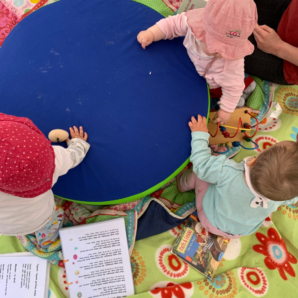 Das Bild zeigt eine Impression von oben auf eine Spielsituation für Kleinkinder. Es sind deri Kleinkinder, Spielzeuge, Liedtexte zu sehen.