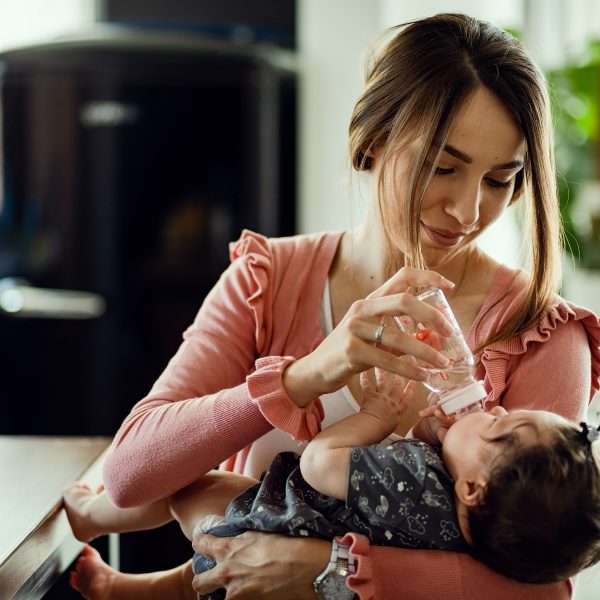 lachelnde mutter die eine babyflasche verwendet und ihrer kleinen tochter wasser gibt 1 - FiZ Leipzig
