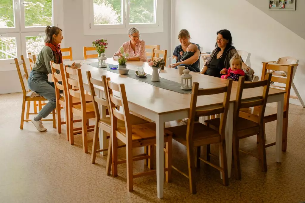 Frauen sitzen mit ihren Kindern am Tisch und lachen.
