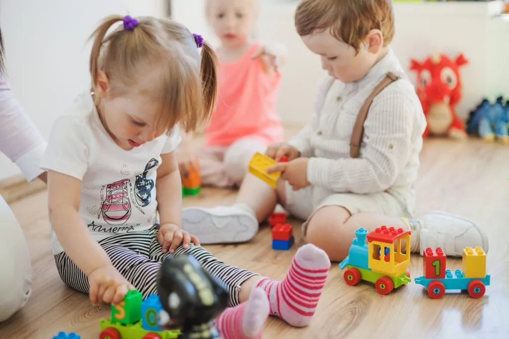 Kleine Kinder spielen auf dem Boden mit einer bunten Eisenbahn.