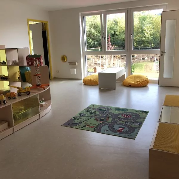 Offener Spielbereich mit Spielzeug-Regalen, Teppich und Sitzgelegenheiten.