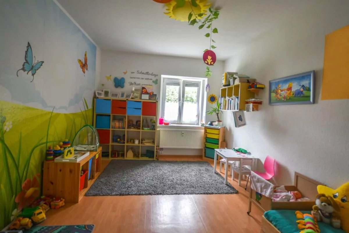 Buntes Kinderzimmer mit Regalen, Spielzeug und Sitzgelegenheiten.