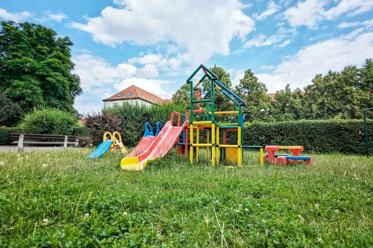 Bunte Kinder-Rutschen, ein Kinder-Kletterturm und eine Kinder-Sitz-Bank stehen in einem grünen Garten.