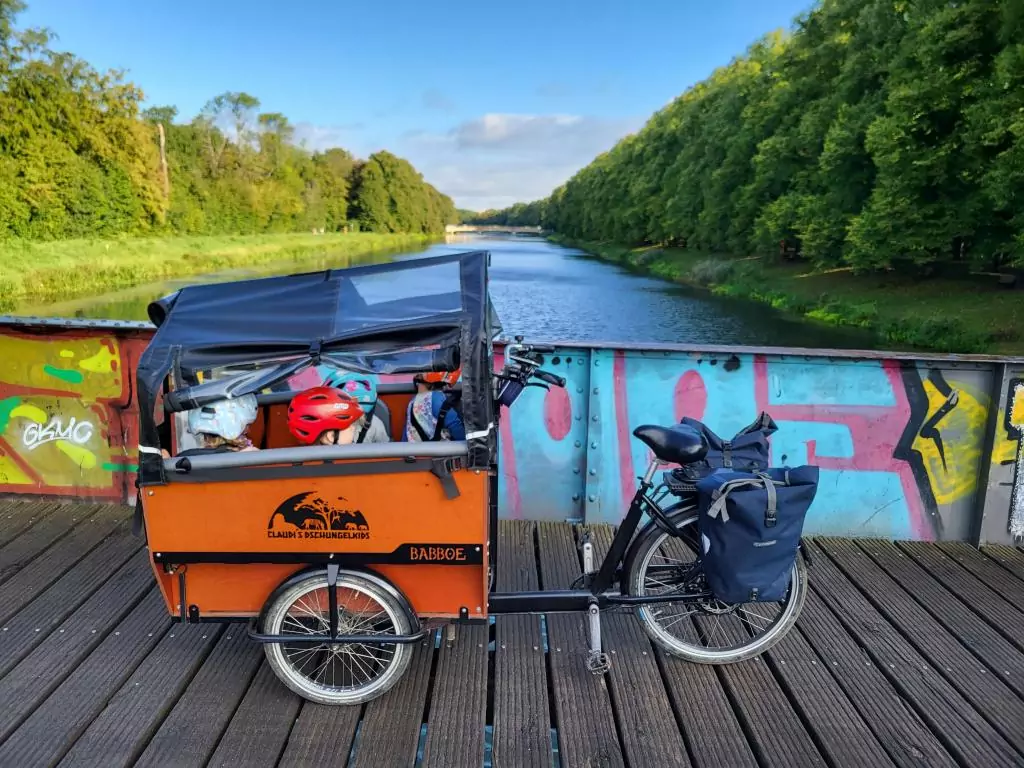 Ein Lastenfahrrad steht auf einer Brücke. Darin sitzen vier Kinder mit Fahrradhelm.