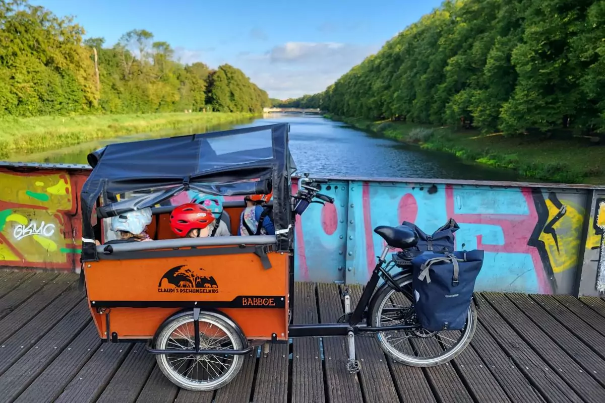 Ein Lastenfahrrad steht auf einer Brücke. Darin sitzen vier Kinder mit Fahrradhelm.