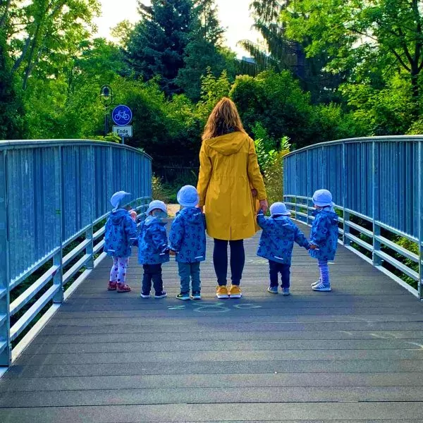 Eine Frau in gelber Jacke steht mit fünf Kindern, jeweils in blau gekleidet, auf einer Brücke.