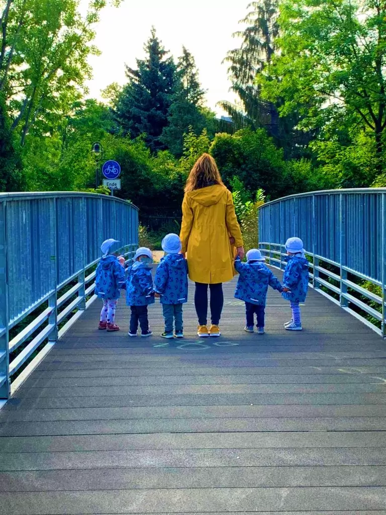 Eine Frau in gelber Jacke steht mit fünf Kindern, jeweils in blau gekleidet, auf einer Brücke.