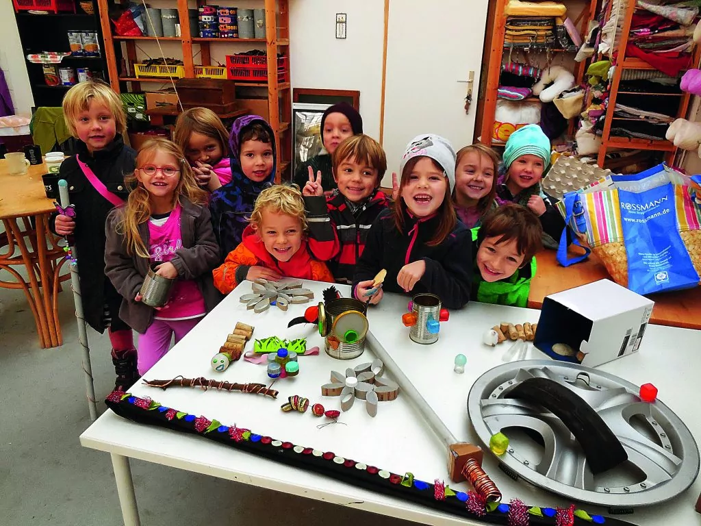 Viele Kinder stehen lächelnd hinter einem Tisch mit Upcycling-Gegenständen.
