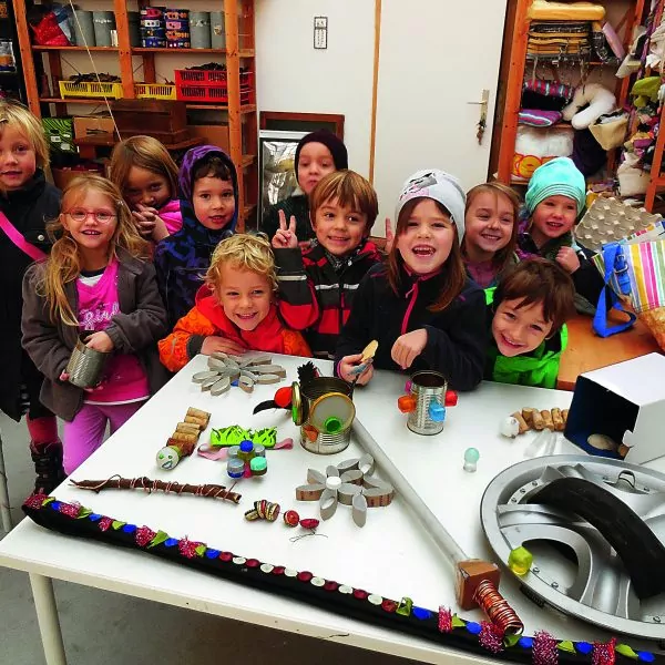 Viele Kinder stehen lächelnd hinter einem Tisch mit Upcycling-Gegenständen.