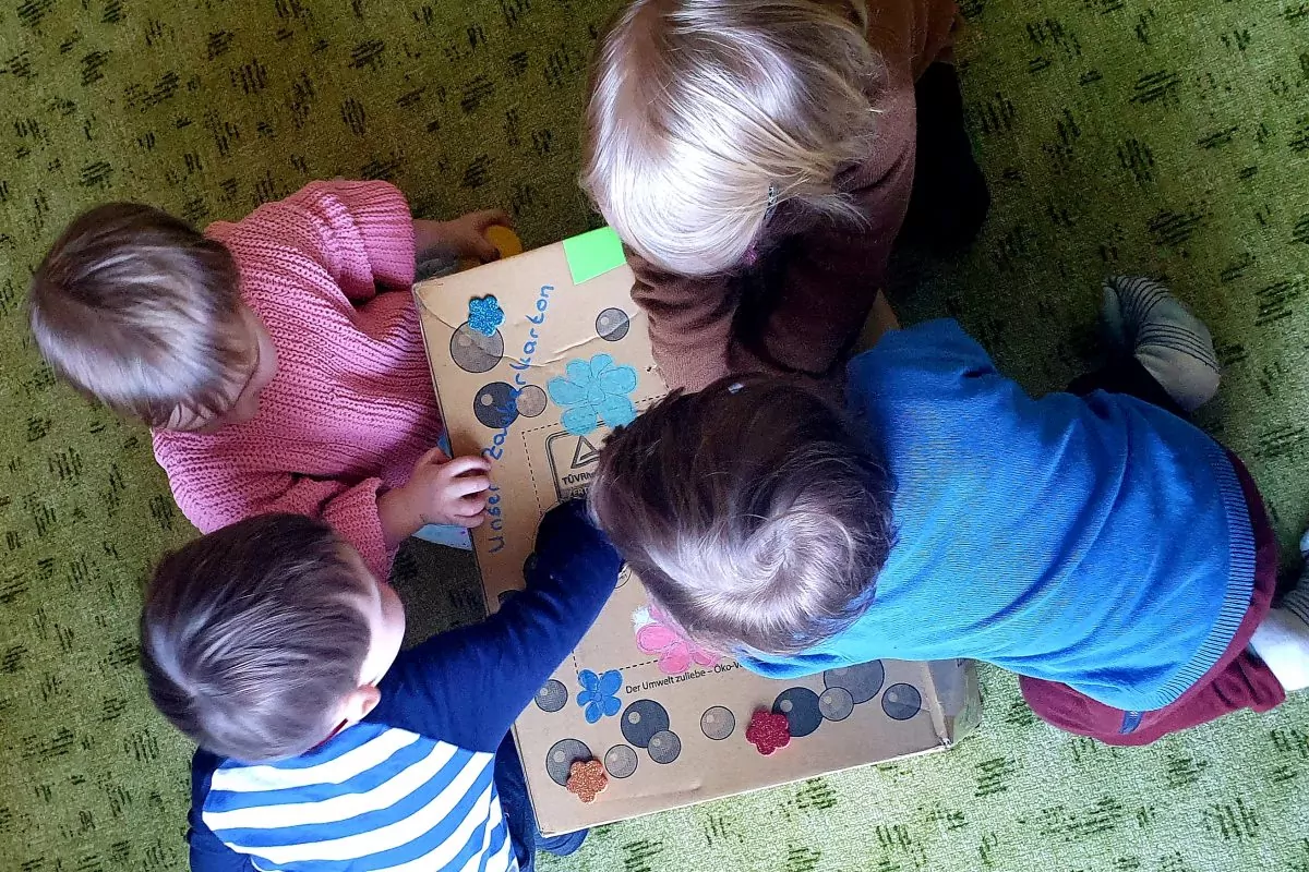 Vier Kinder spielen mit einem buntem Karton.